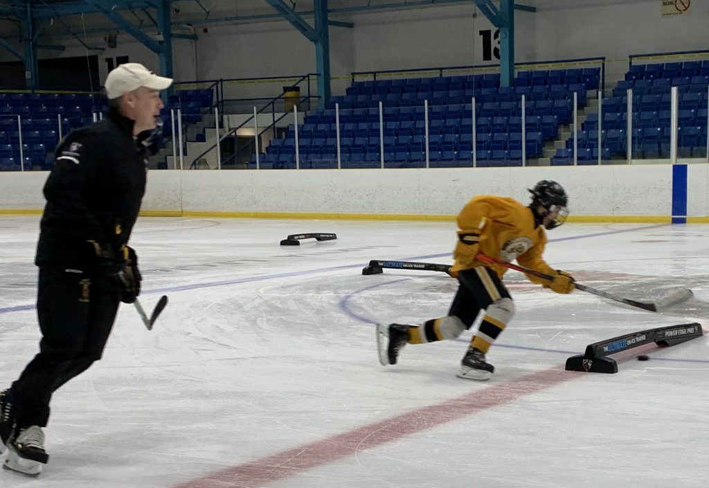 Photo of a hockey coach supporting a player on the ice with skills development.