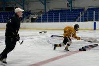 Photo of a hockey coach supporting a player on the ice with skills development.
